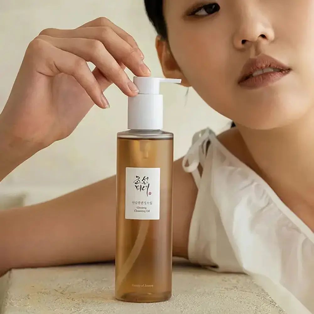 Donna che tiene in mano un flacone. Sul flacone, testo coreano e "Cleansing Oil".