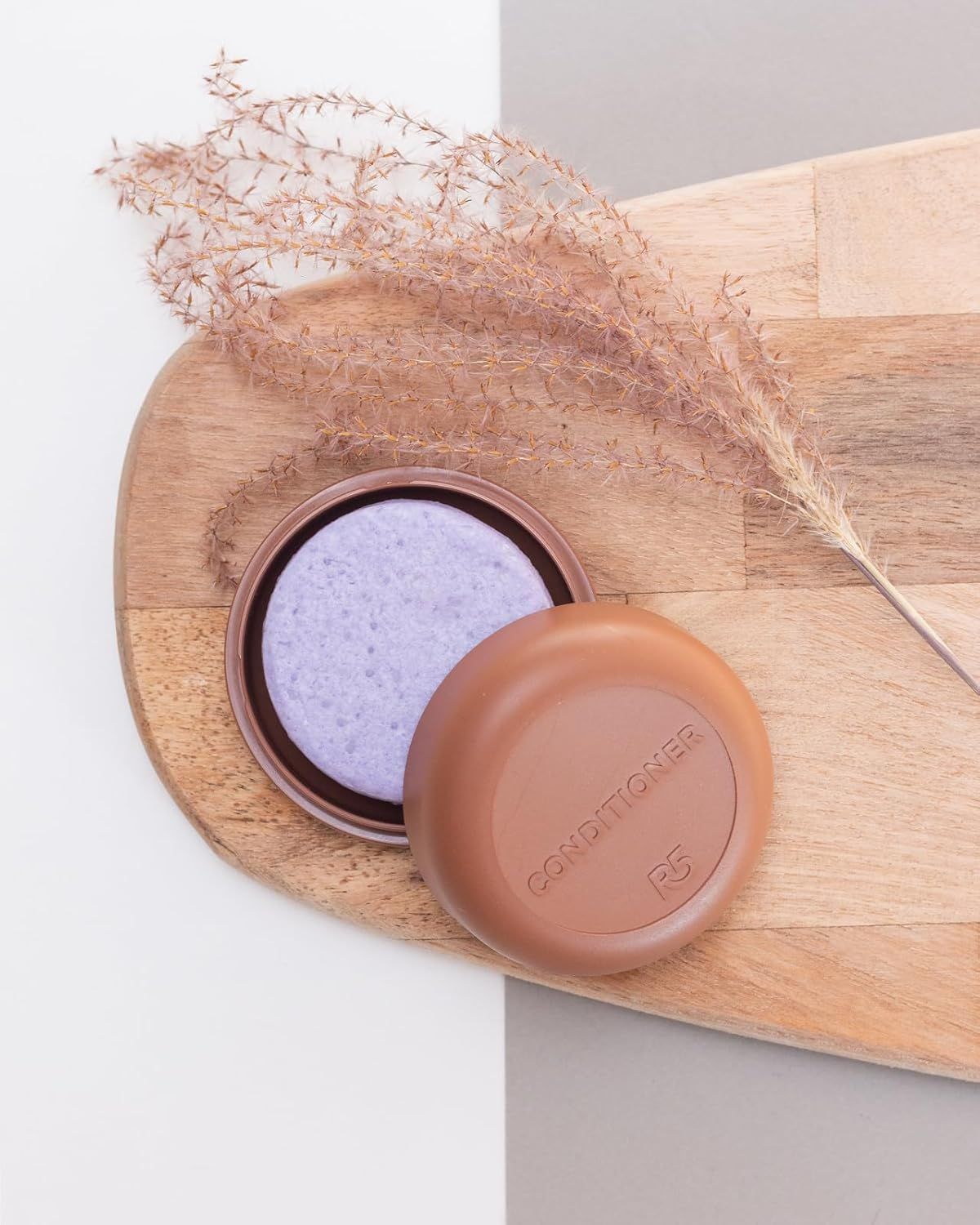 Contenitore rotondo marrone con balsamo viola. Su tavola di legno con pianta.