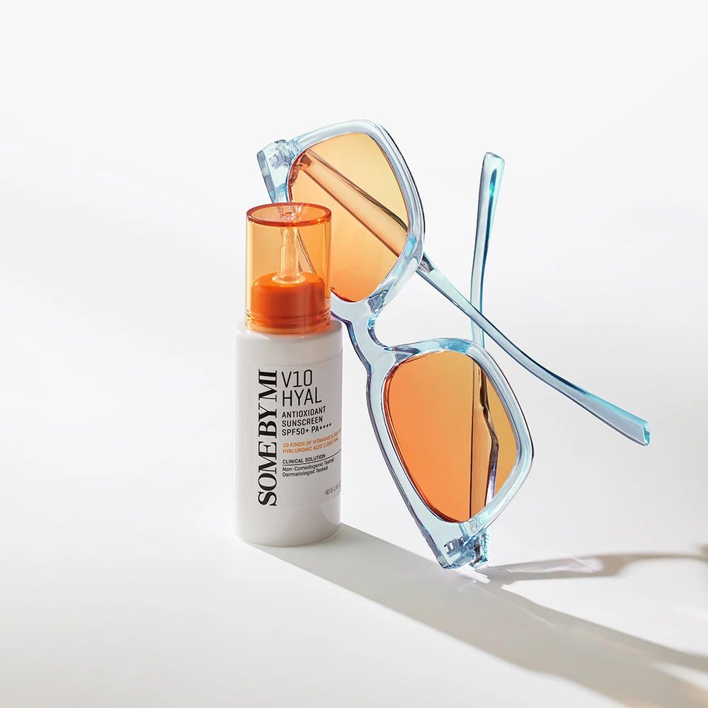 Flacone bianco con tappo arancione e occhiali da sole. Scritta: V10 Hyal Antioxidant Sunscreen SPF 50+ PA++++.