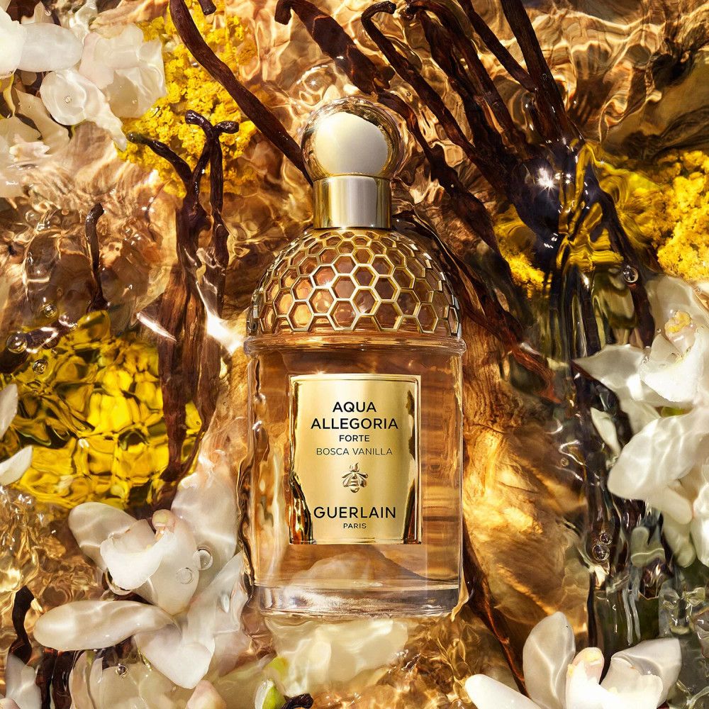 Flacone di profumo a nido d'ape. Etichetta: Aqua Allegoria Forte Bosca Vanilla, Guerlain Paris. Circondato da fiori e baccelli di vaniglia.