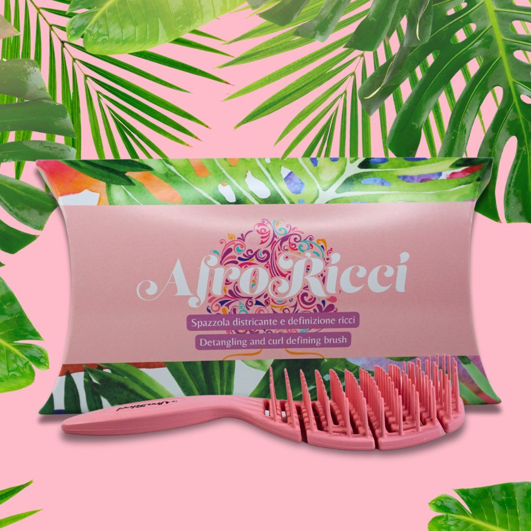 Spazzola rosa e confezione con testo: "AfroRicci Spazzola districante e definizione ricci". Sfondo: foglie.