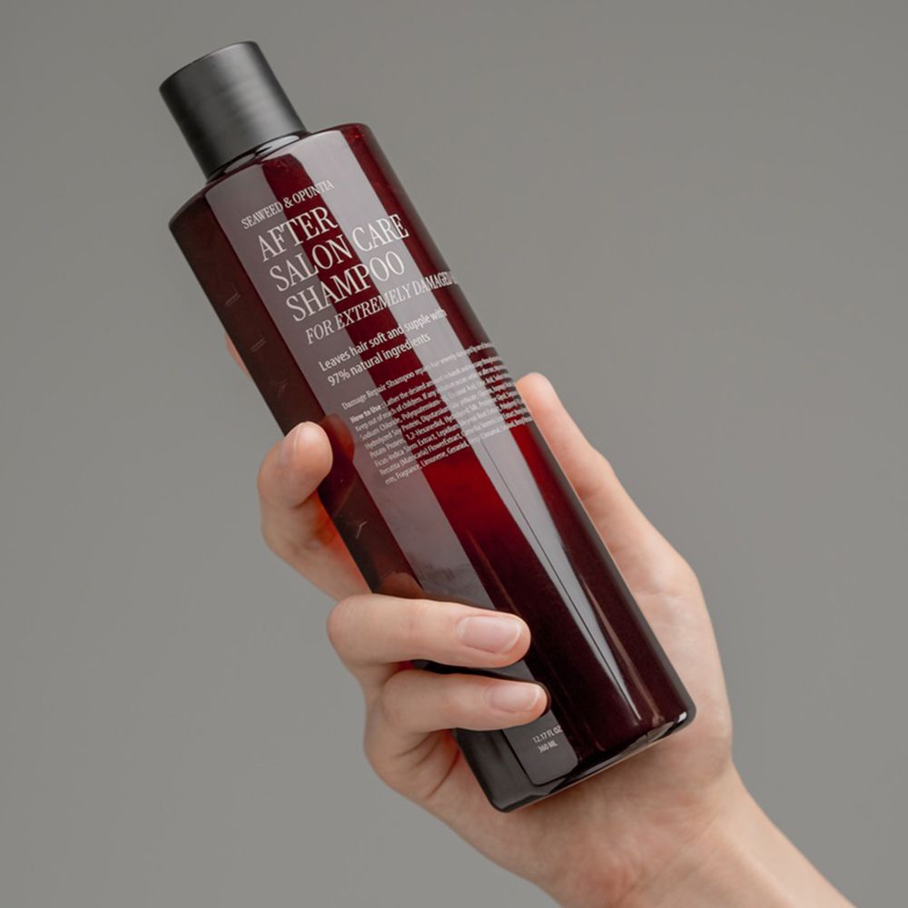 Mano che tiene un flacone di shampoo rosso con tappo nero. Scritta: After Salon Care Shampoo per capelli estremamente danneggiati.