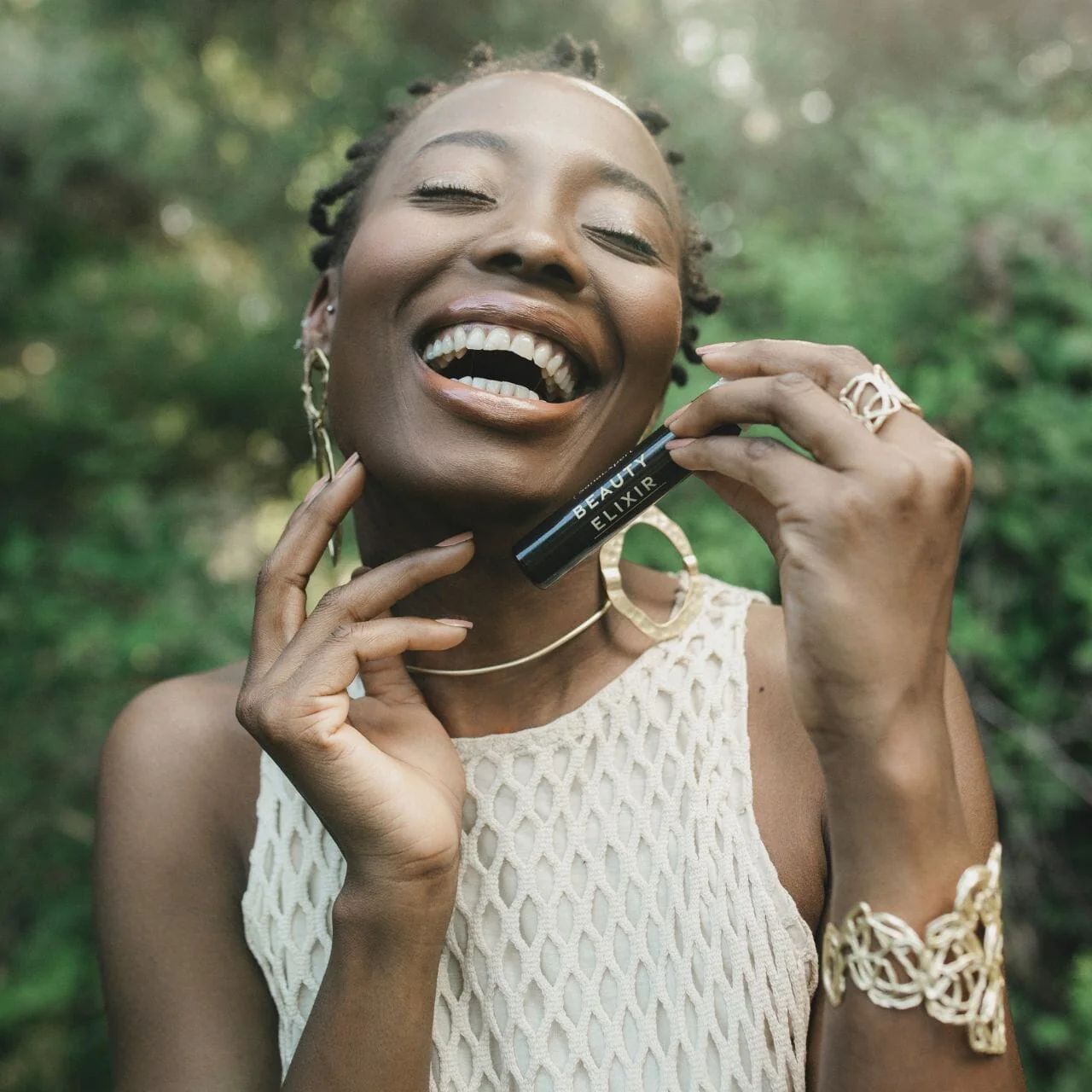 Donna sorridente con fiala « BEAUTY ELIXIR ». Gioielli dorati.