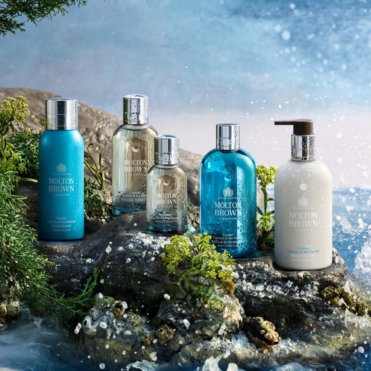 Diverse bottiglie su una roccia davanti all'acqua. Logo Molton Brown sulle bottiglie.