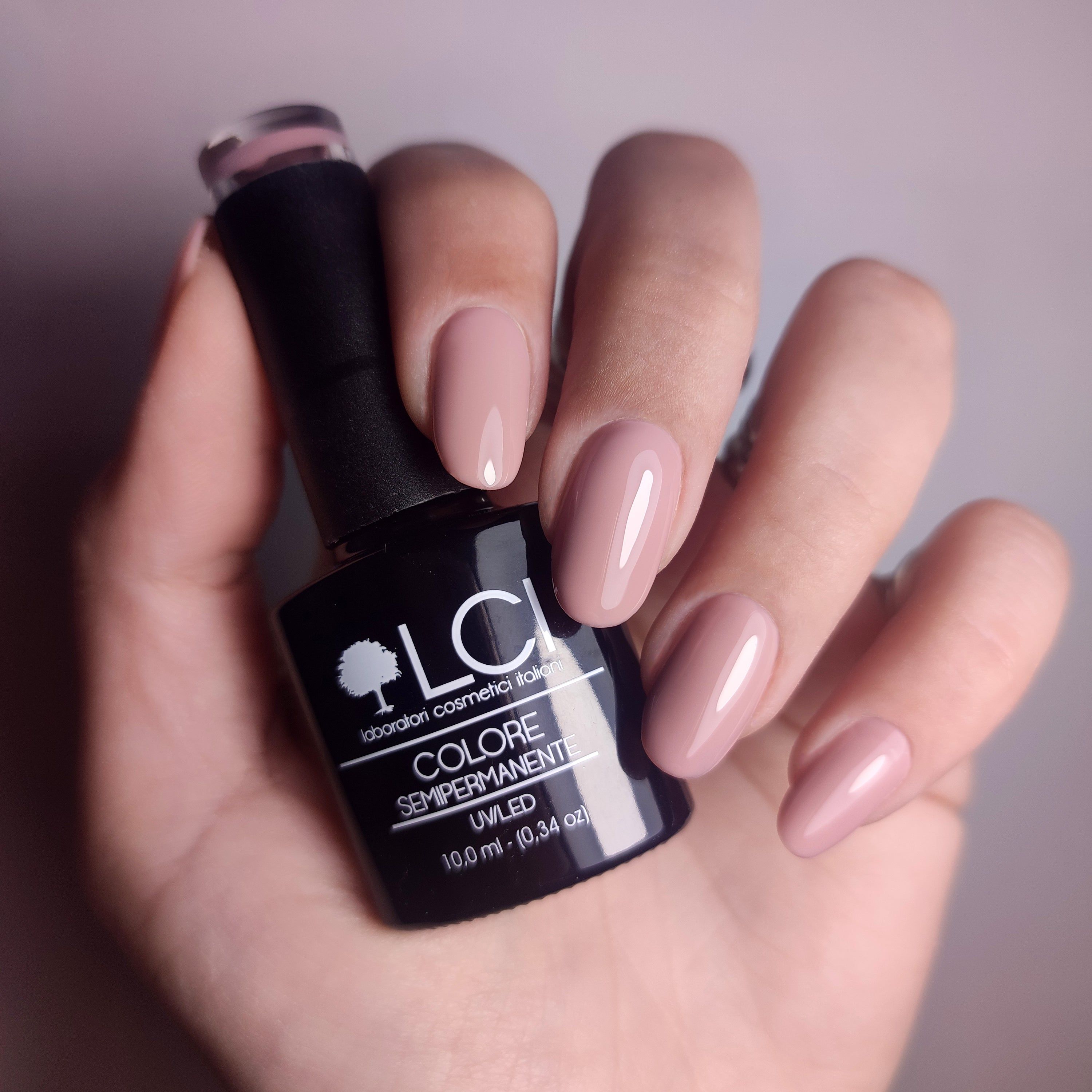 Mano con unghie smaltate e flacone di smalto. Scritta: LCI, COLORE SEMIPERMANENTE. Unghie e smalto rosa.