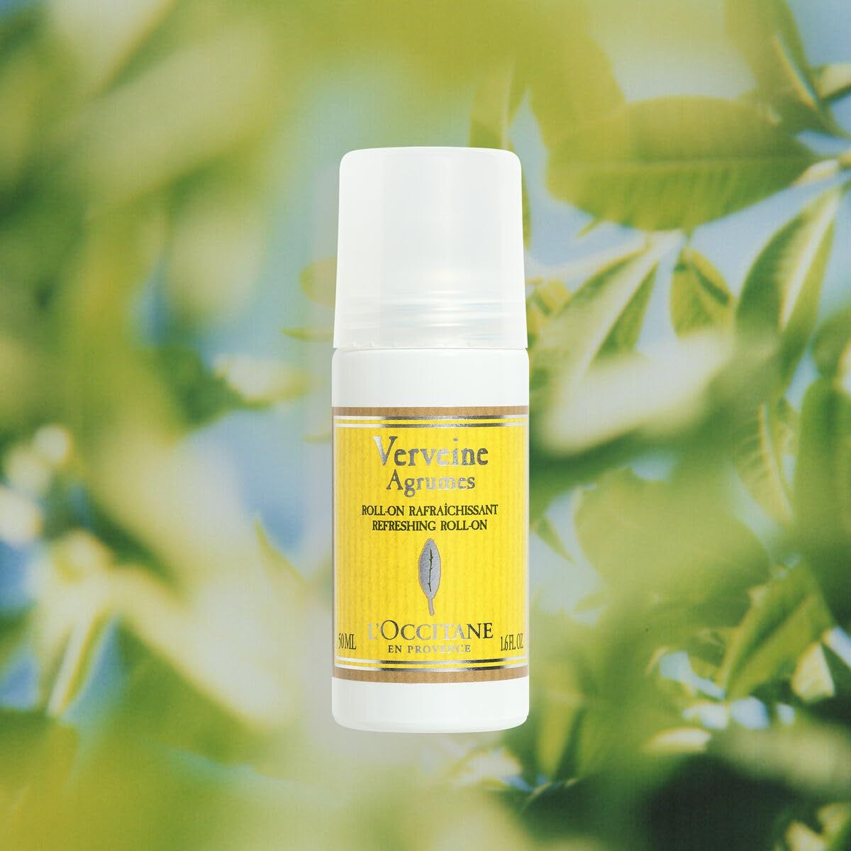 Deodorante roll-on con tappo bianco. Etichetta gialla con testo: "Verveine Agrumes", "L'Occitane". Sfondo: foglie verdi.