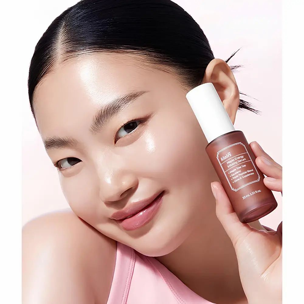 Donna tiene in mano una bottiglia marrone. Scritta: Klairs Maple Energy Infusing Serum. 30 ml.