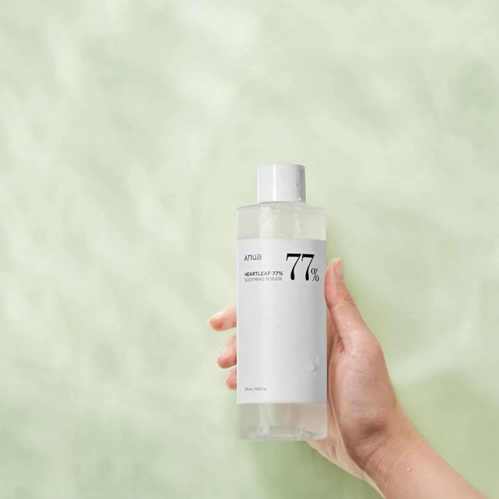 Mano che tiene un flacone con tappo bianco. Sfondo verde chiaro. Scritta: Anua, Heartleaf 77% Soothing Toner.