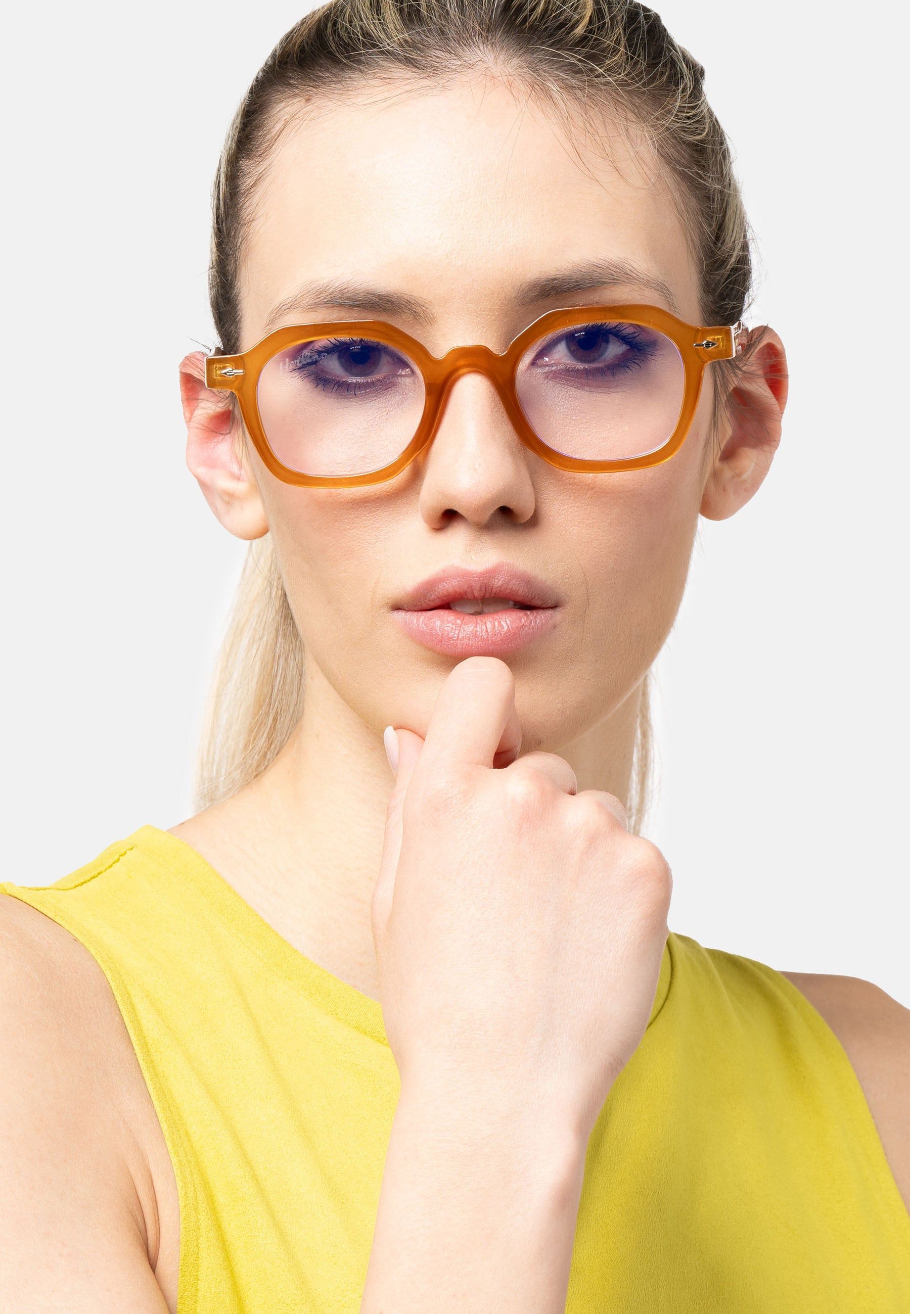 Donna con occhiali color miele. Montatura angolare. Top giallo. Sguardo verso l'alto.