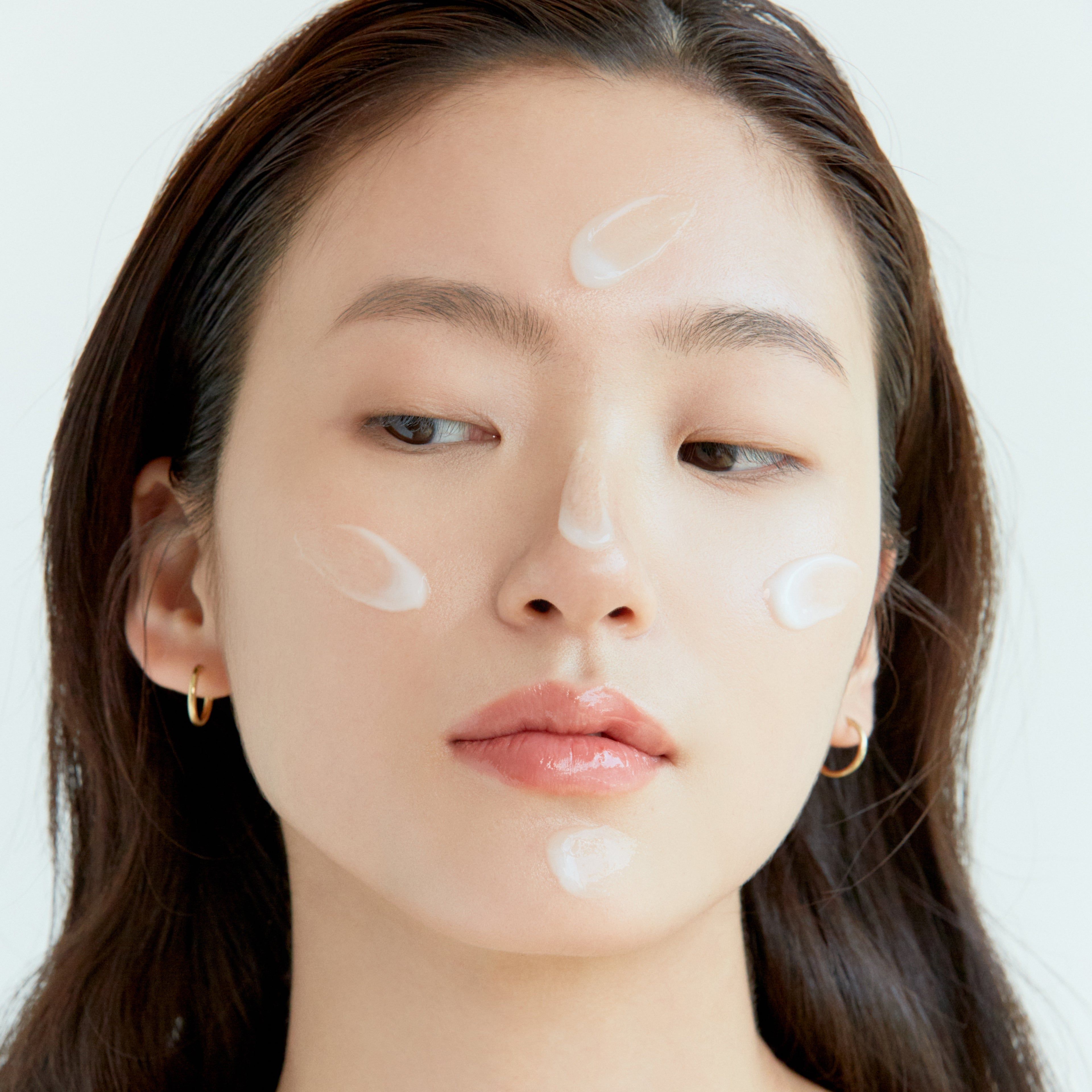 Viso di donna con punti di crema sulla pelle. Nessun packaging del prodotto visibile.