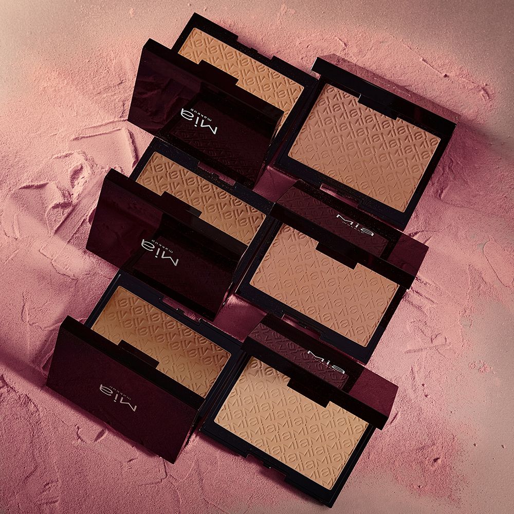 Diverse confezioni di Mia Makeup Tan Builder Matte Bronzer. I compatti quadrati neri sono aperti, mostrando il bronzer marrone chiaro. Il nome del marchio Mia Makeup è visibile sui coperchi.