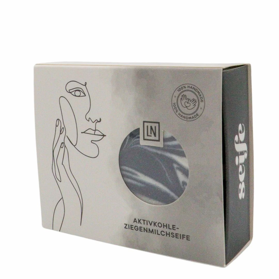 Sapone in scatola. Sapone nero con vortici bianchi visibili attraverso una finestra. Scritta: Aktivkohle-Ziegenmilchseife.