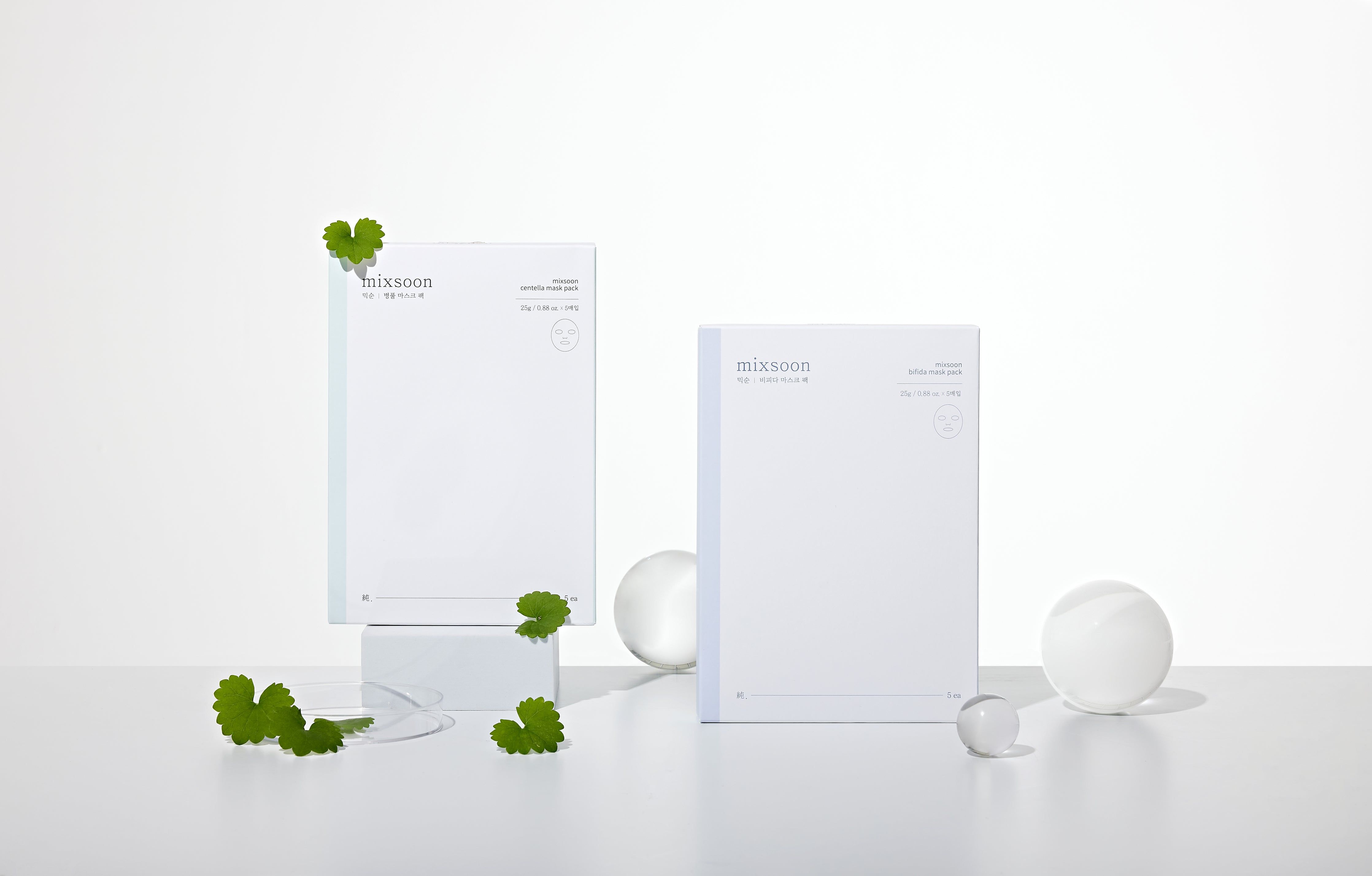 Due confezioni Mixsoon Centella Mask Pack. Pacchi bianchi rettangolari. Accanto, foglie verdi e sfere trasparenti.
