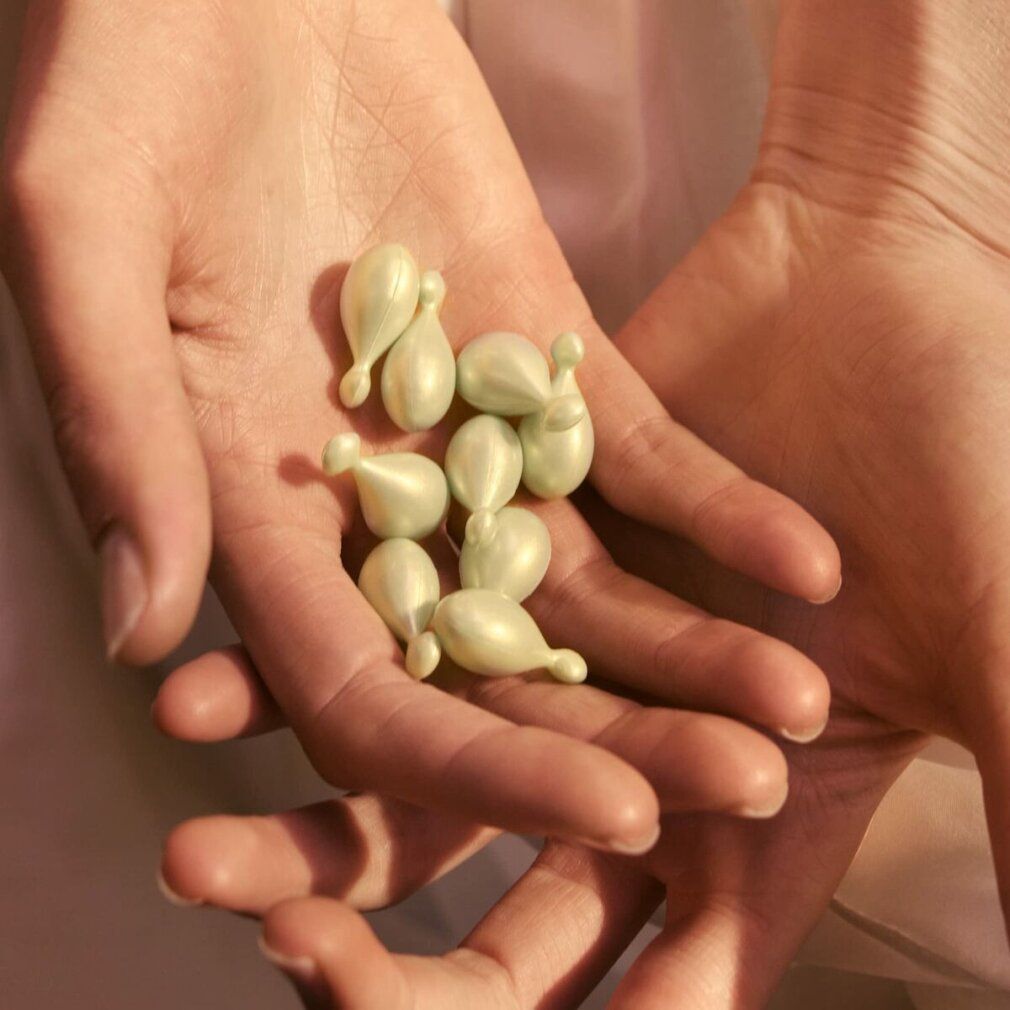 Mani che tengono una piccola quantità di capsule verdi a forma di goccia.