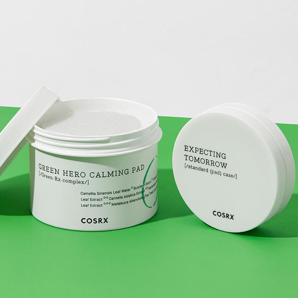 Contenitore bianco con cuscinetti e coperchio. Scritta: Green Hero Calming Pad, COSRX. Sfondo verde.