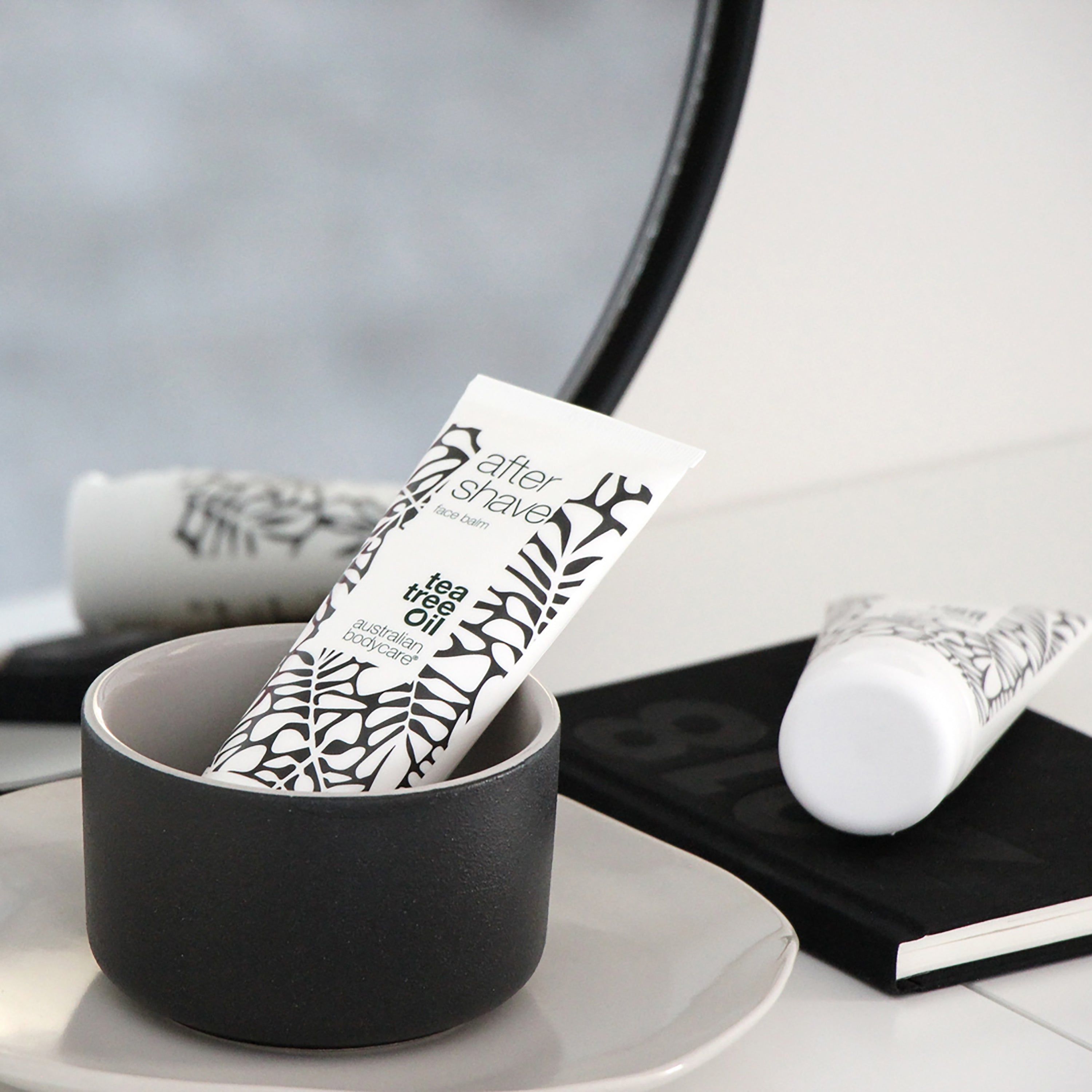 Balsamo dopobarba in una ciotola nera. Scritta: After Shave, Tea Tree Oil, Australian Bodycare. Taccuino nero.