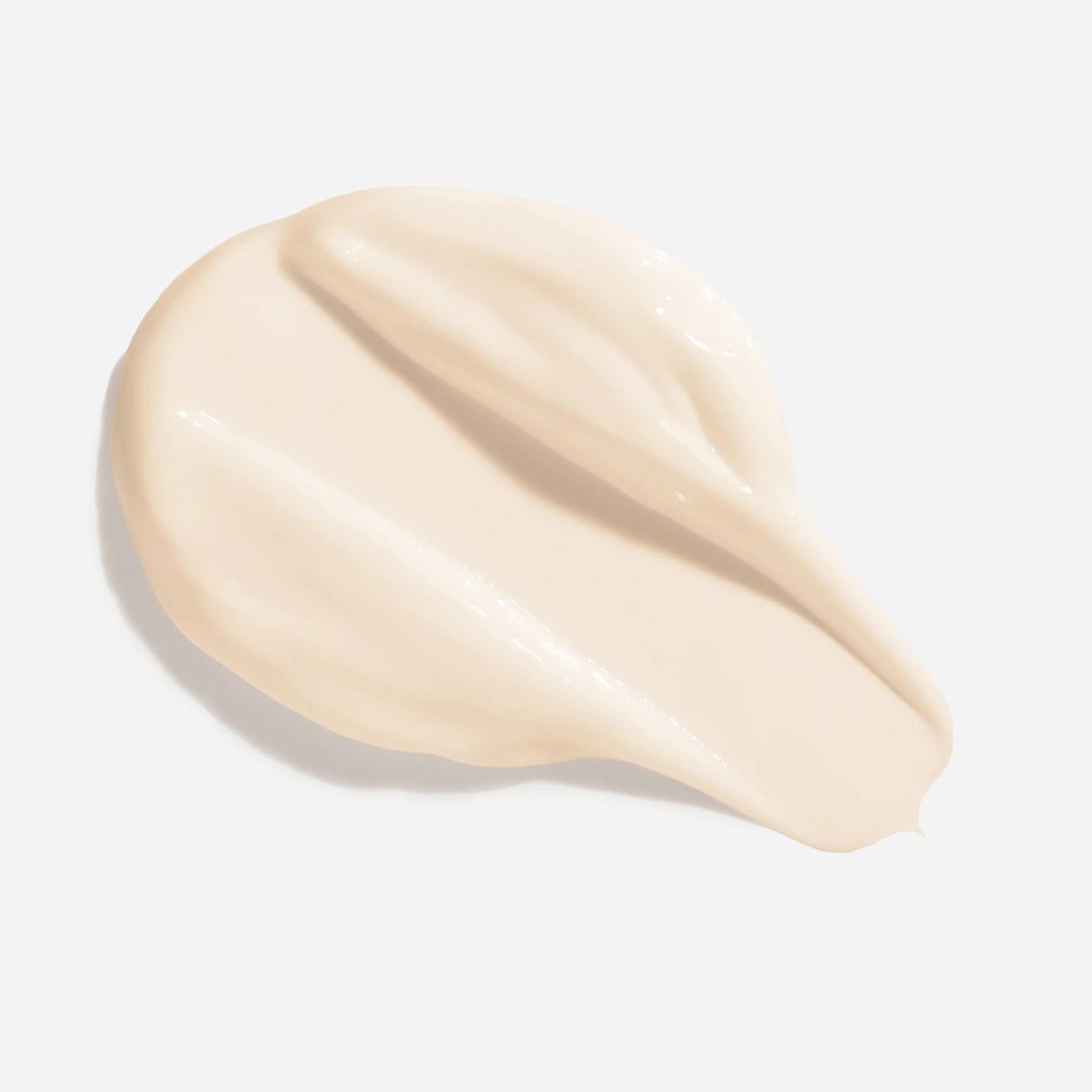 Campione di crema su sfondo bianco. La crema è beige chiaro e ha una consistenza liscia e lucida.