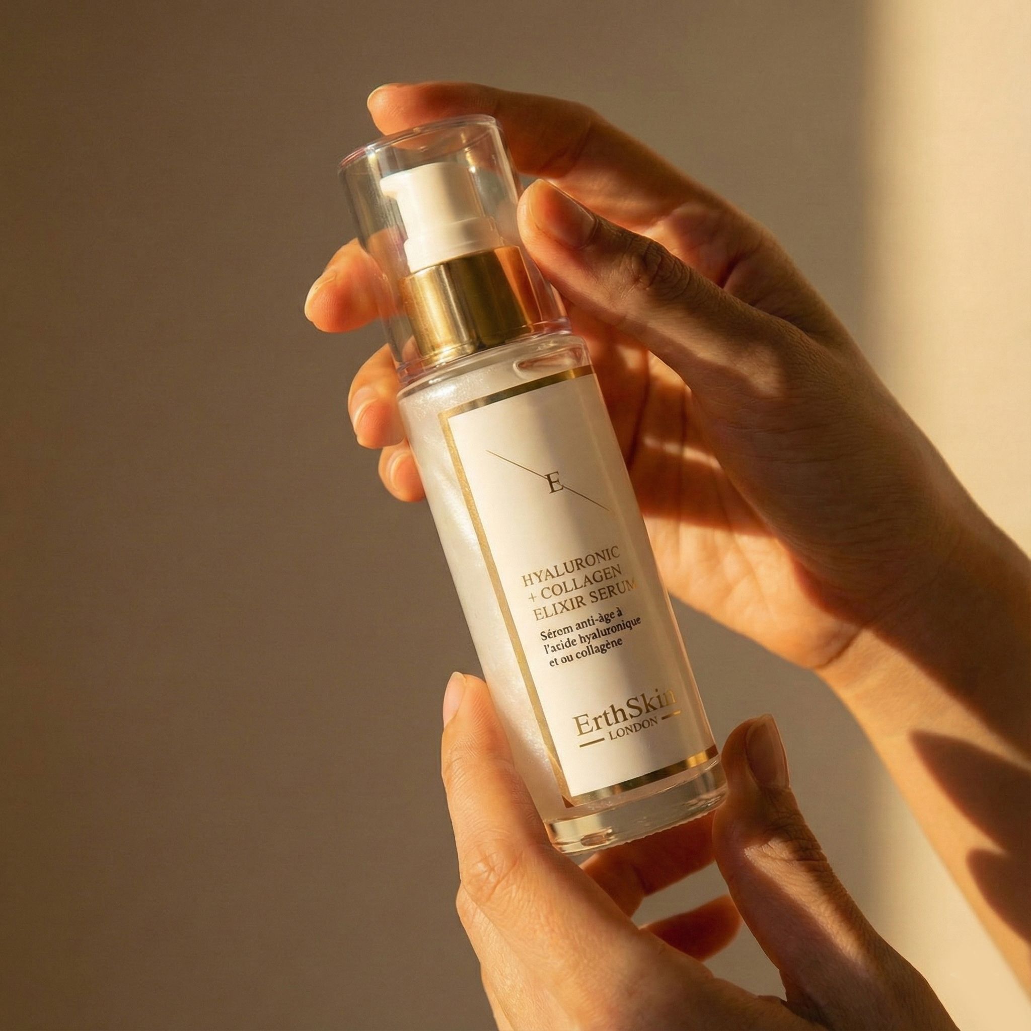 Mani che tengono un flacone di Siero Elisir Acido Ialuronico + Collagene ErthSkin London.