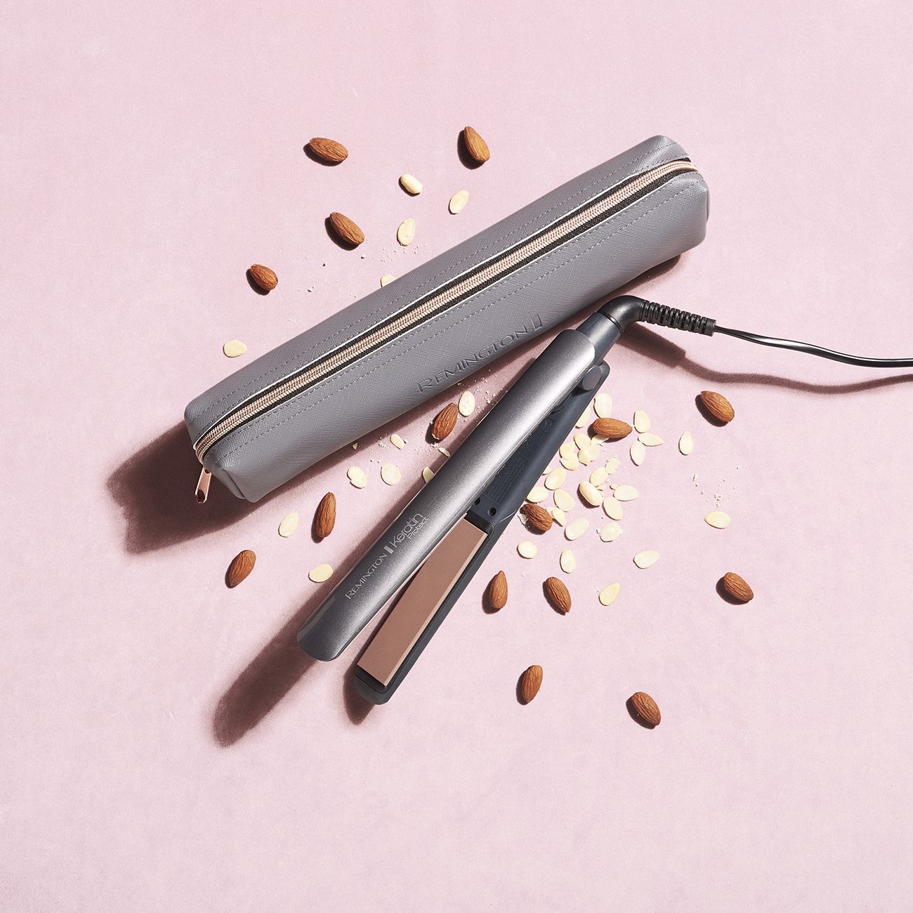 Piastra per capelli cheratina e custodia grigia. Mandorle su sfondo rosa.