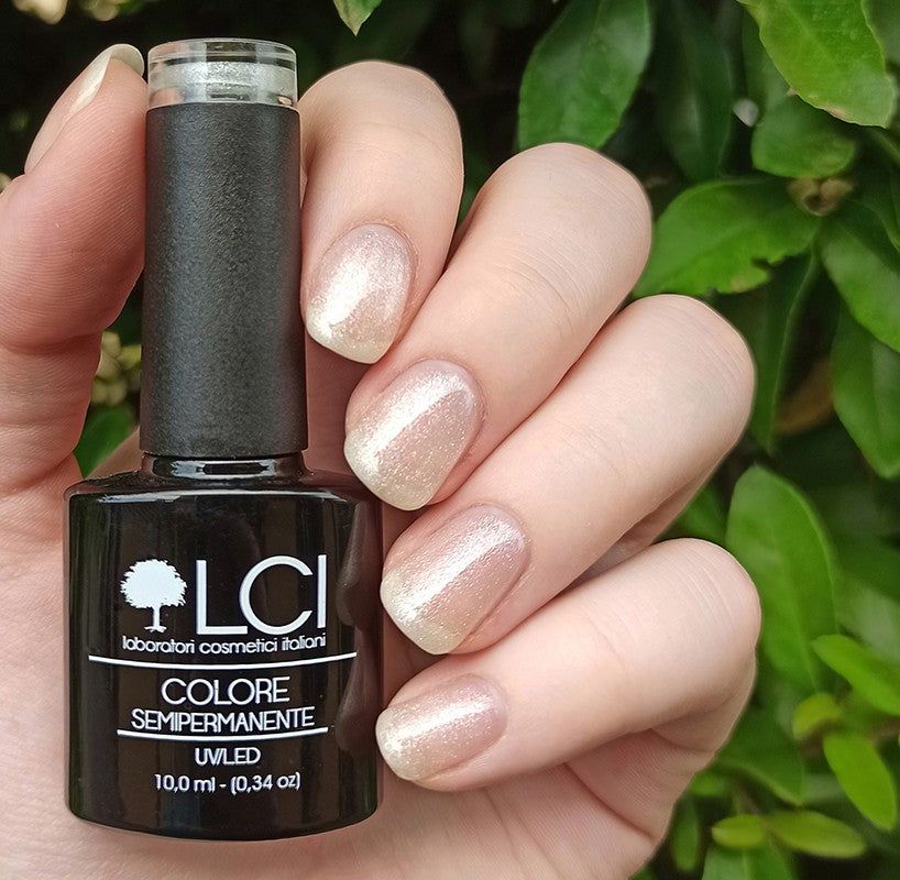 Flacone di smalto accanto a unghie smaltate. Flacone nero con etichetta bianca. Unghie con smalto glitterato.