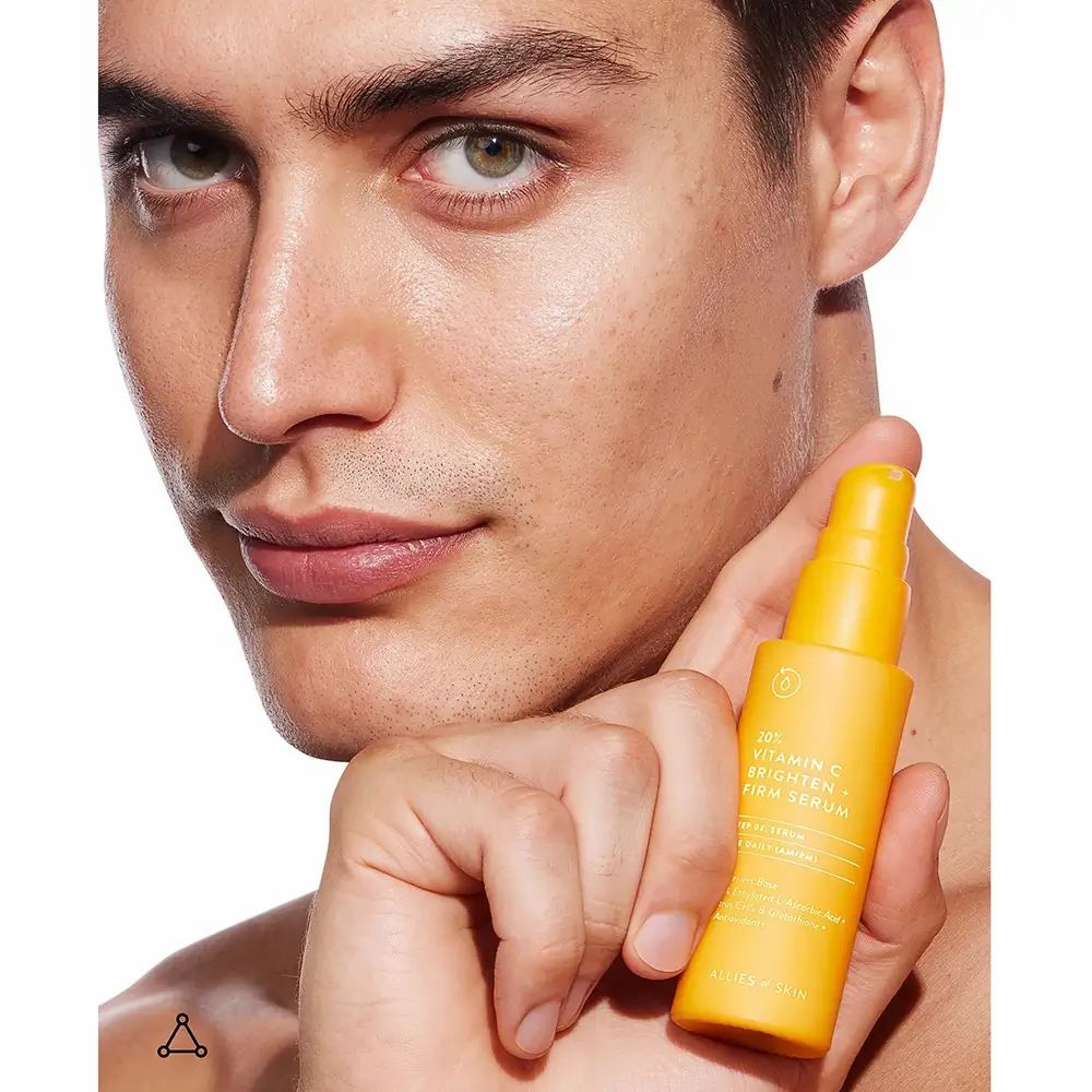 Uomo con siero giallo. Scritta: 20% Vitamin C Brighten + Firm Serum. Marchio: ALLIES OF SKIN.