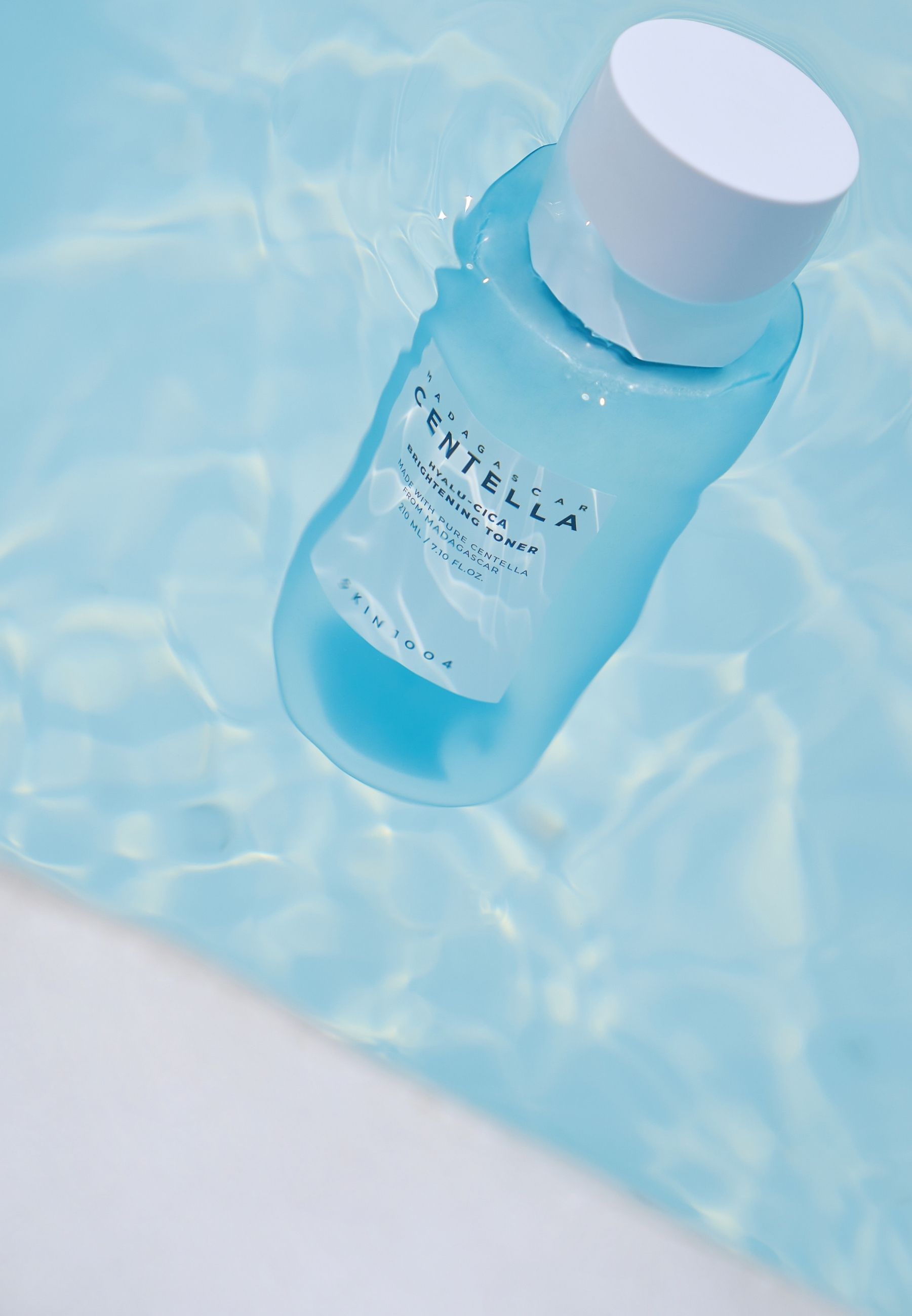 Flacone blu chiaro nell'acqua. Tappo bianco. Testo: CENTELLA, HYALU-CICA, Brightening Toner. SKIN1004.