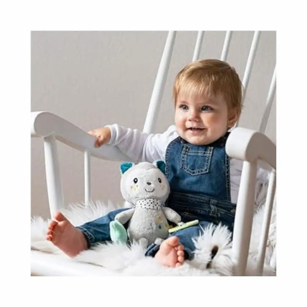 Bambino seduto su una sedia a dondolo con peluche grigio. Peluche con orecchie blu, sciarpa a pois, stella, specchio e sonaglio.