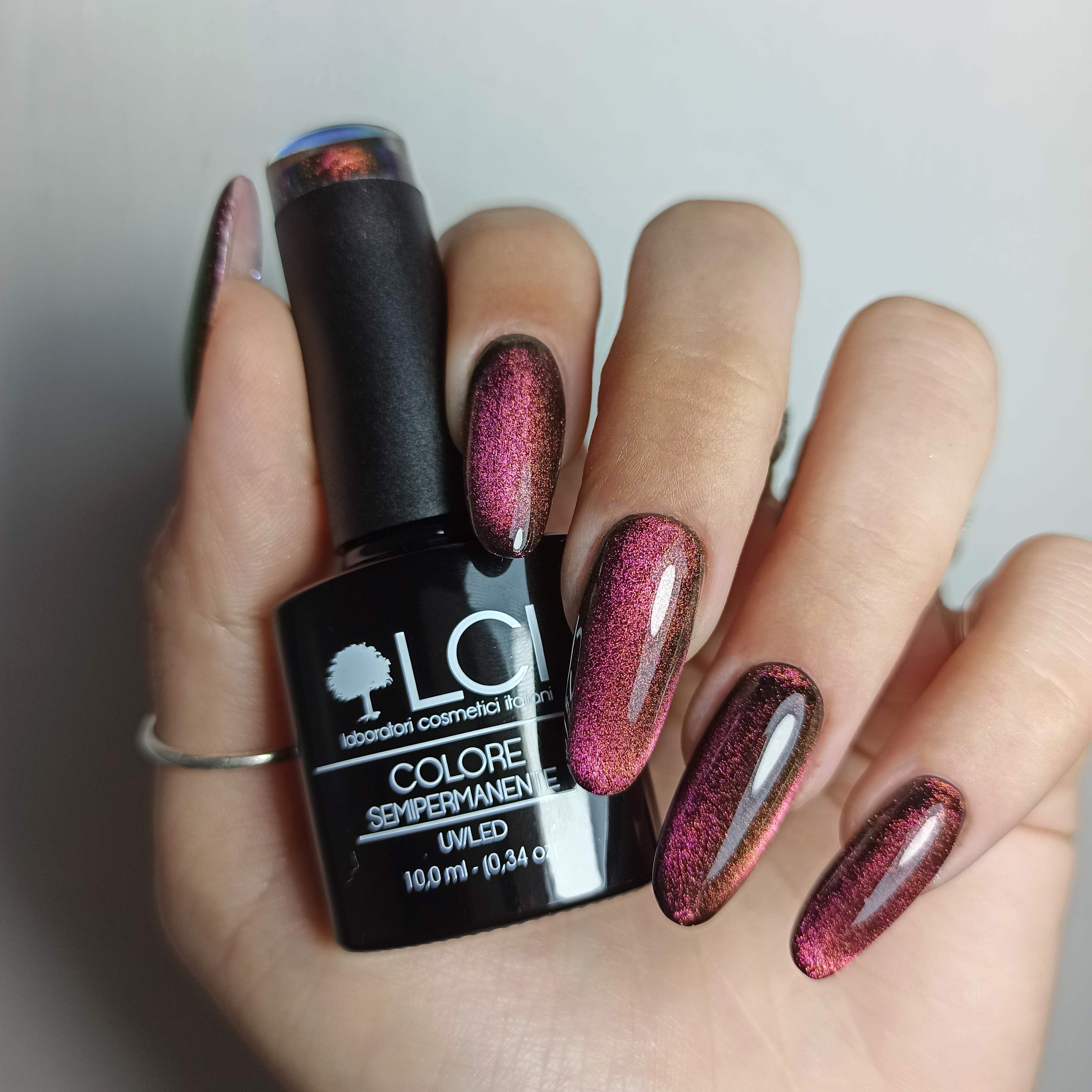 Mano con unghie smaltate. Flacone di smalto con tappo nero. Unghie con effetto 5D Cat Eye.