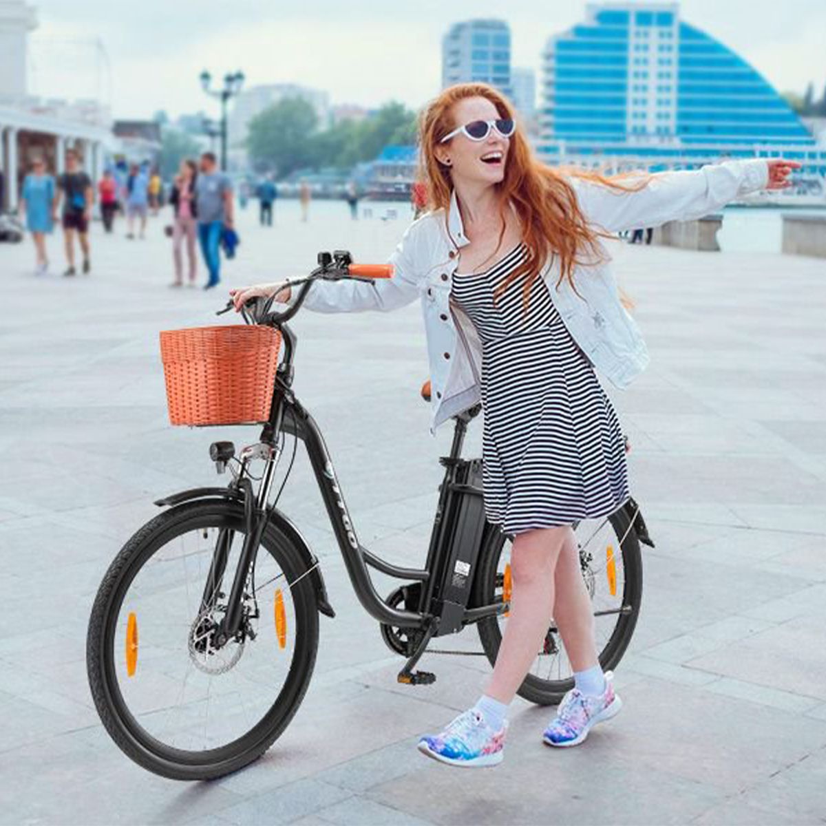 Donna con bicicletta elettrica nera. Cestino, sella marrone, manopole arancioni. Logo TTGO.