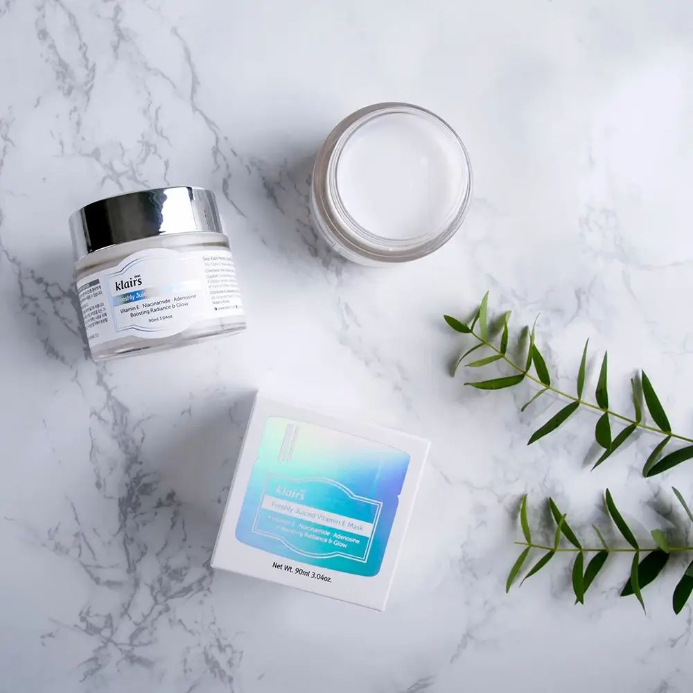 Tre prodotti su sfondo marmoreo: vaso di crema, vaso aperto, scatola. Pianta.