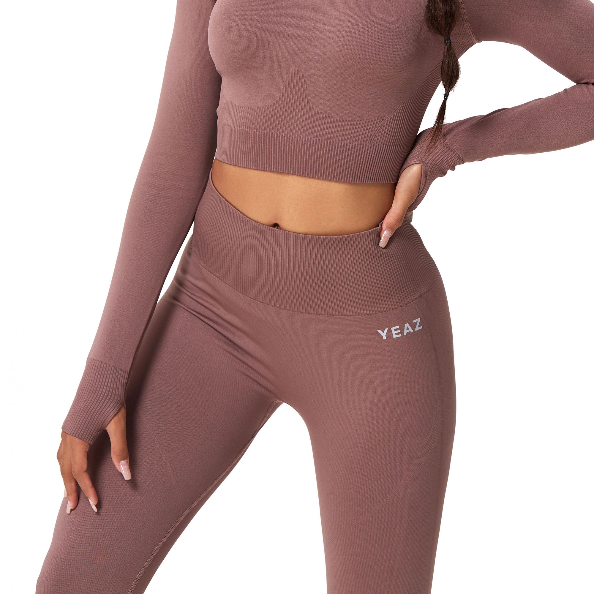Completo sportivo in due pezzi color malva, con crop top a maniche lunghe e leggings con foro per il pollice e logo del marchio.