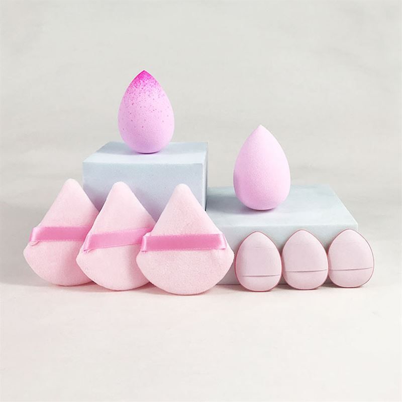 Diverse spugne per trucco di forme e colori vari. Alcune a goccia, altre triangolari con nastri. Collocate su piedistalli.