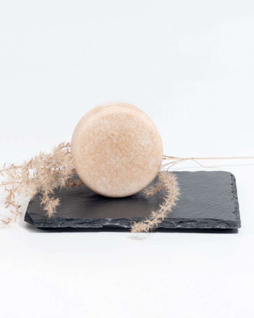 Shampoo solido rotondo su ardesia nera. Fiori secchi accanto.