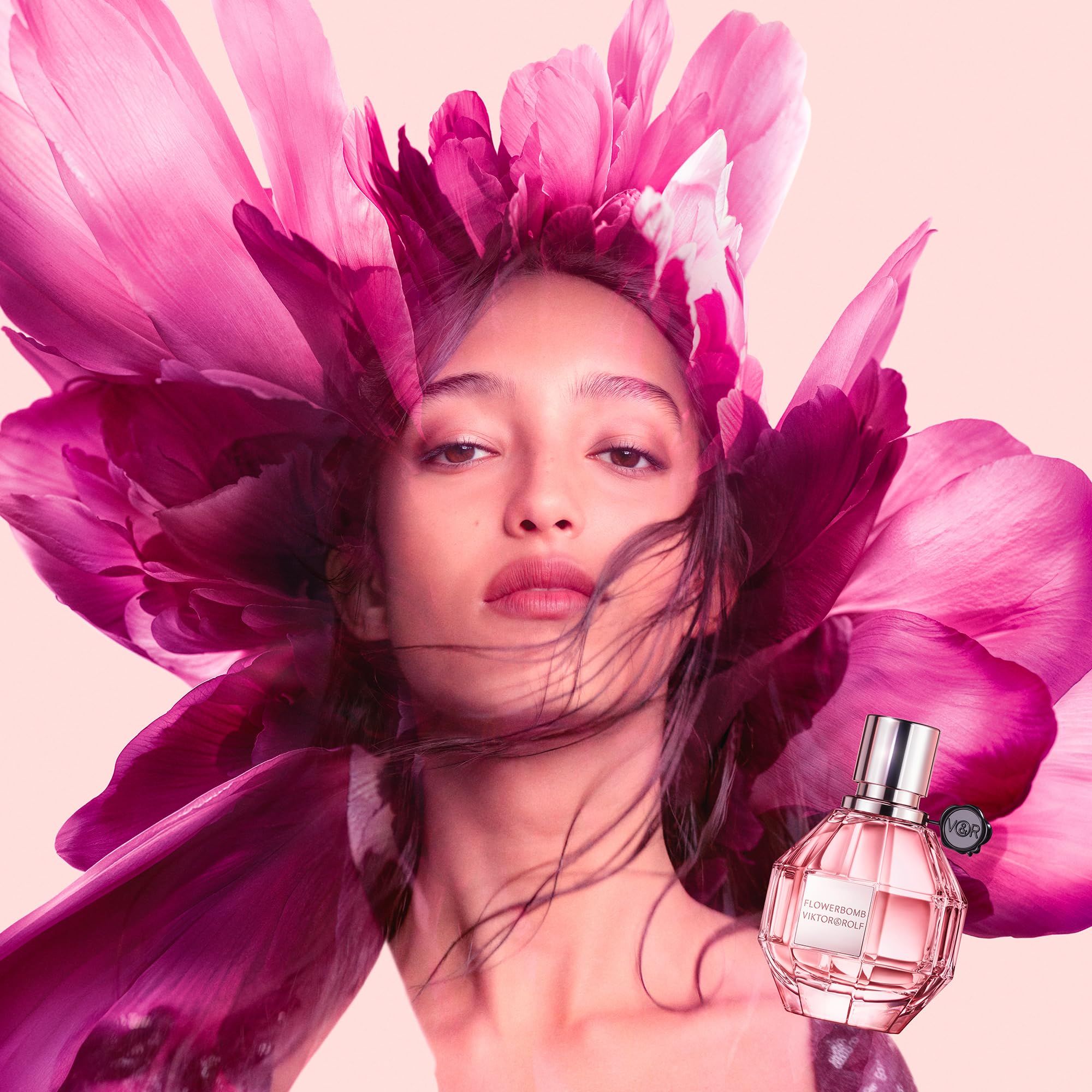 Donna con copricapo floreale e flacone di profumo Flowerbomb di Viktor & Rolf. Sfondo rosa. Flacone in basso a destra.