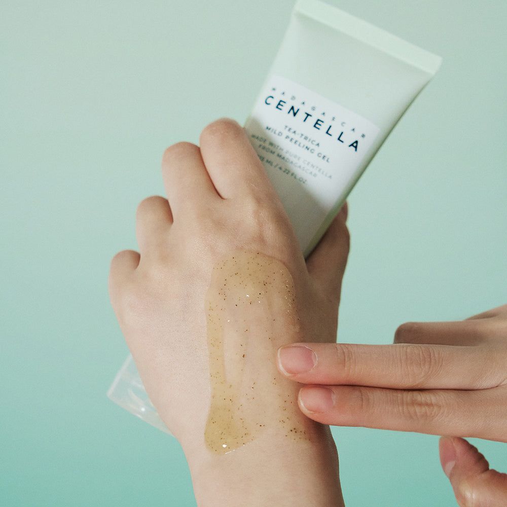 Mani che tengono un tubo verde. Gel sulla mano. Testo: MADAGASCAR CENTELLA, Tea-Trica Mild Peeling Gel.