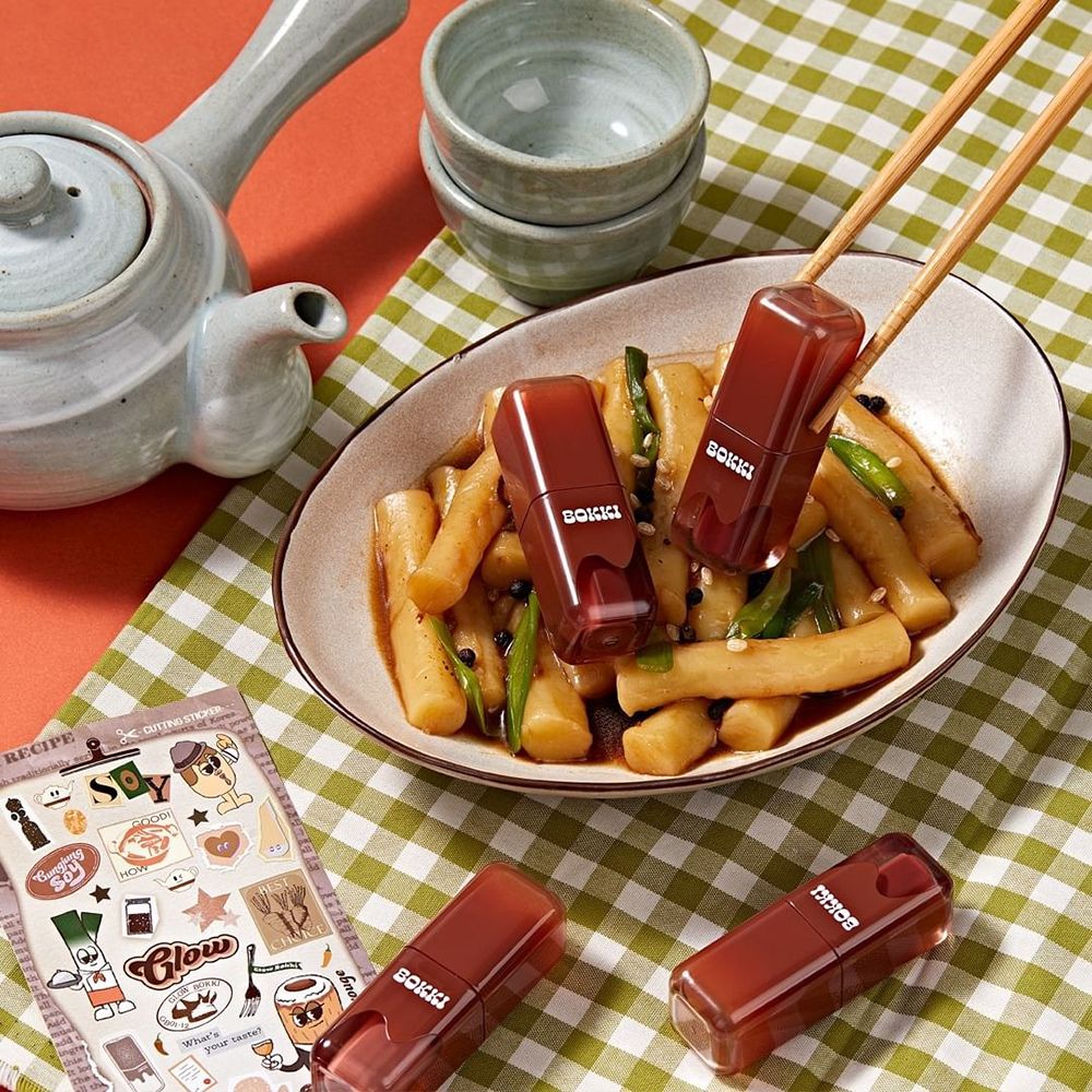Tre lucidalabbra su un piatto di cibo. Due sono tenuti con le bacchette. Scritta: BOKKI.