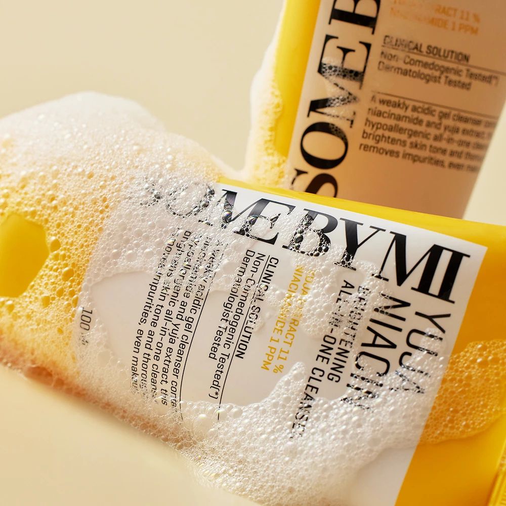 Due tubi gialli con etichetta bianca nella schiuma di sapone. Scritta: Yuja Niacin Brightening All-in-One Cleanser.