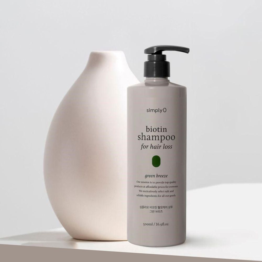 Flacone di shampoo grigio con dosatore nero. Scritta: Biotin Shampoo for hair loss, Green Breeze. Accanto a un vaso.