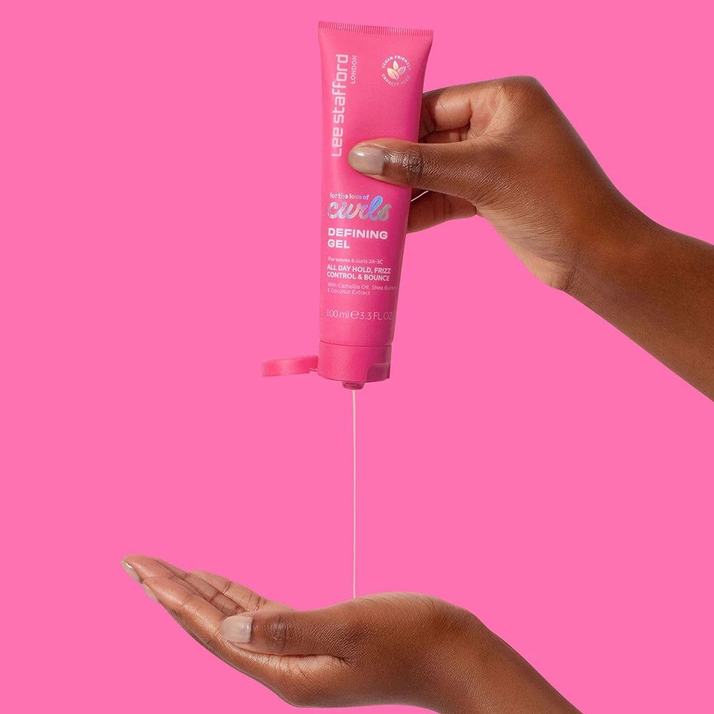 Mano che preme Lee Stafford For The Love Of Curls Defining Gel da un tubetto rosa nel palmo.