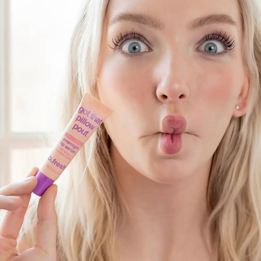 Donna tiene tubo 'Got That Pillow Pout'. Nome prodotto e marchio visibili. Espressione del viso con labbra a becco.