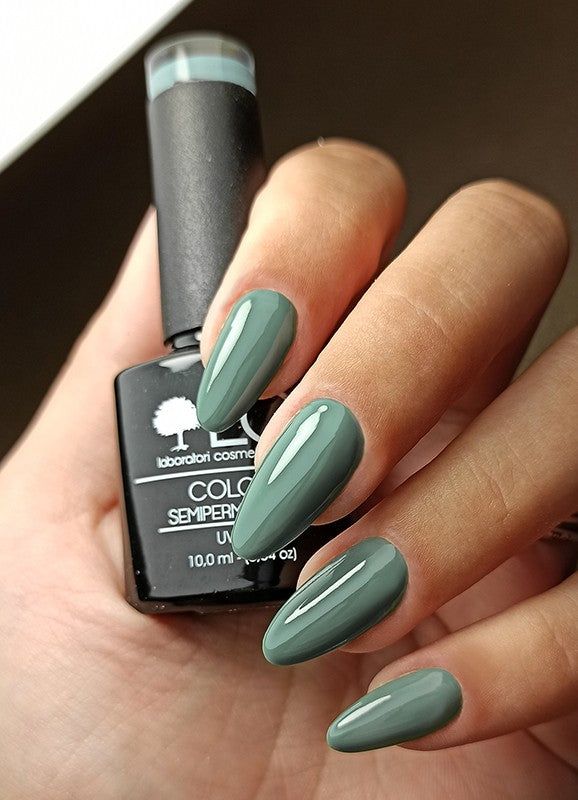 Mano con unghie smaltate e flacone di smalto. Unghie verdi, flacone con scritta: LCI, Colore Semipermanente.