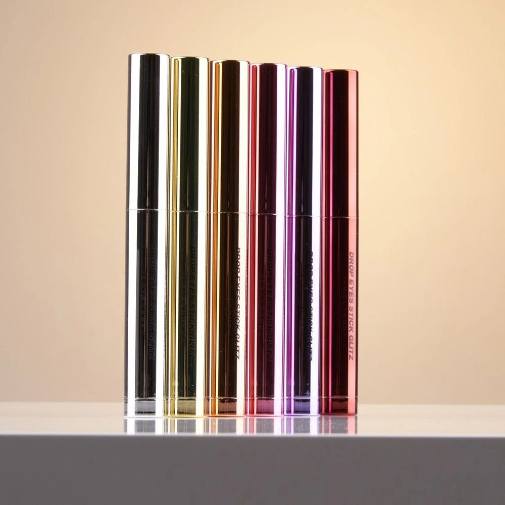 Sei ombretti Drop Eyes Stick Glitz di diversi colori, in fila. Scritta: Drop Eyes Stick Glitz.