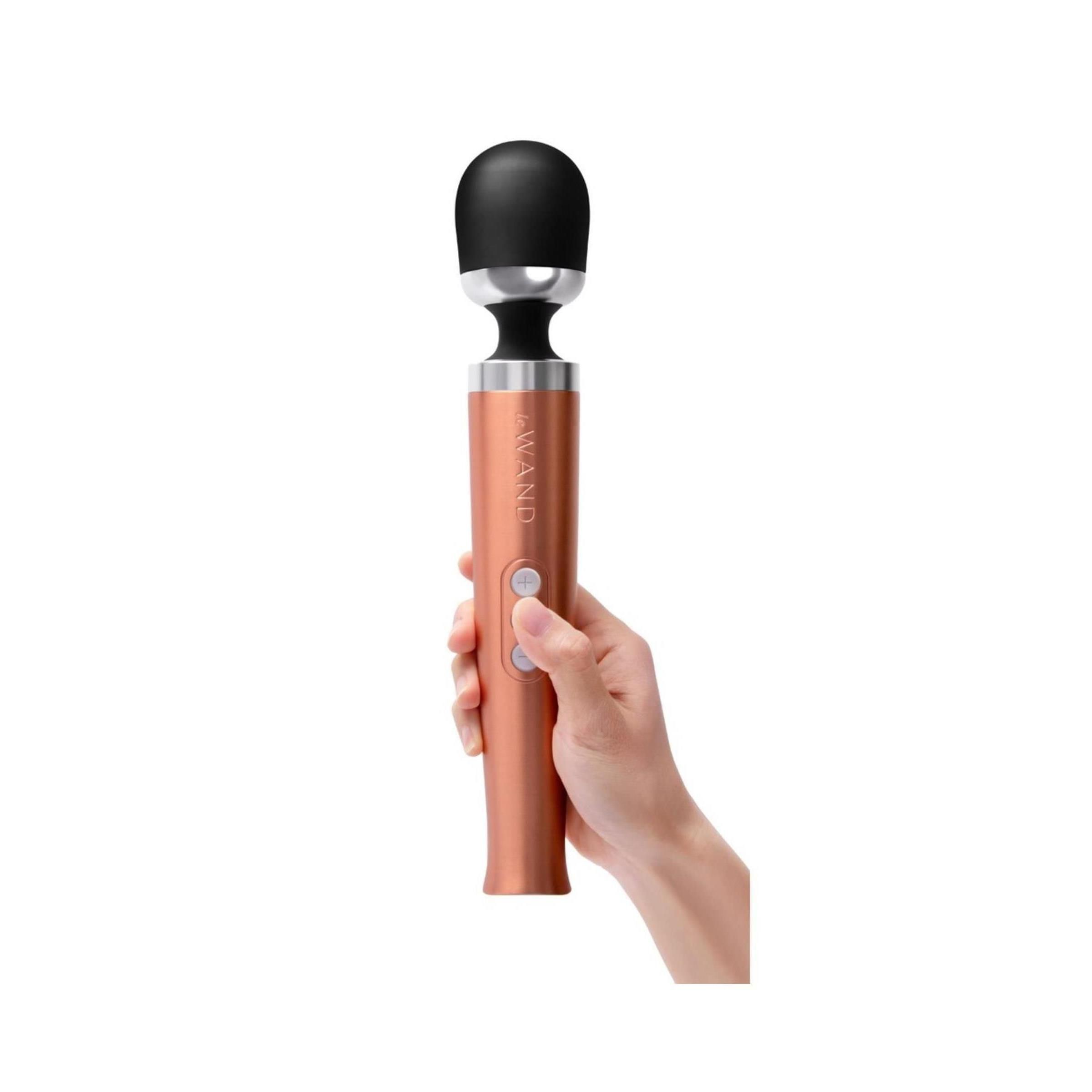 Mano che tiene un massaggiatore color oro rosa con testa nera. Tre pulsanti visibili. Il testo "Le Wand" è riconoscibile.