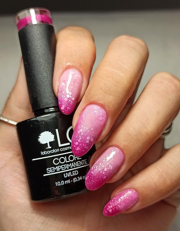 Mano con unghie smaltate e flacone di smalto. Sfumatura rosa con glitter. Scritta: LCI, COLORE SEMIPERMANENTE, UVLED 10,0 ml.