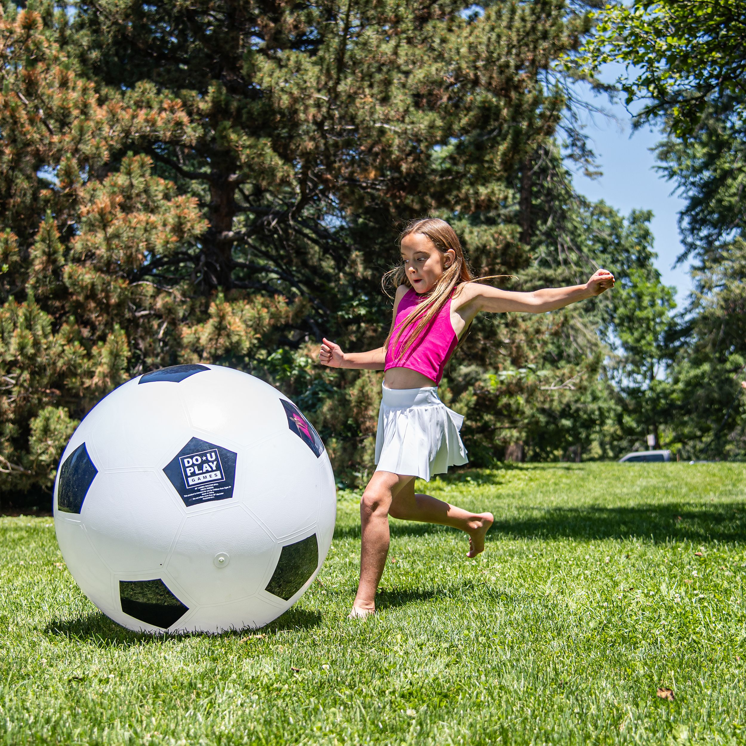Una ragazza calcia un grande pallone da calcio bianco con pentagoni neri su un prato.