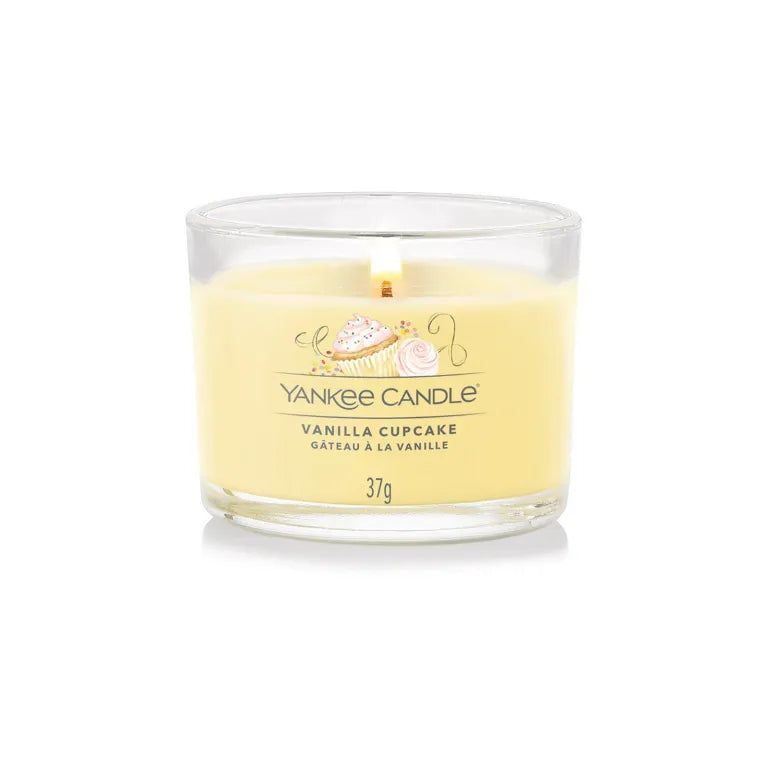 Candela in vetro con cera gialla. Scritta: Yankee Candle Vanilla Cupcake, 37g. Fiamma accesa.