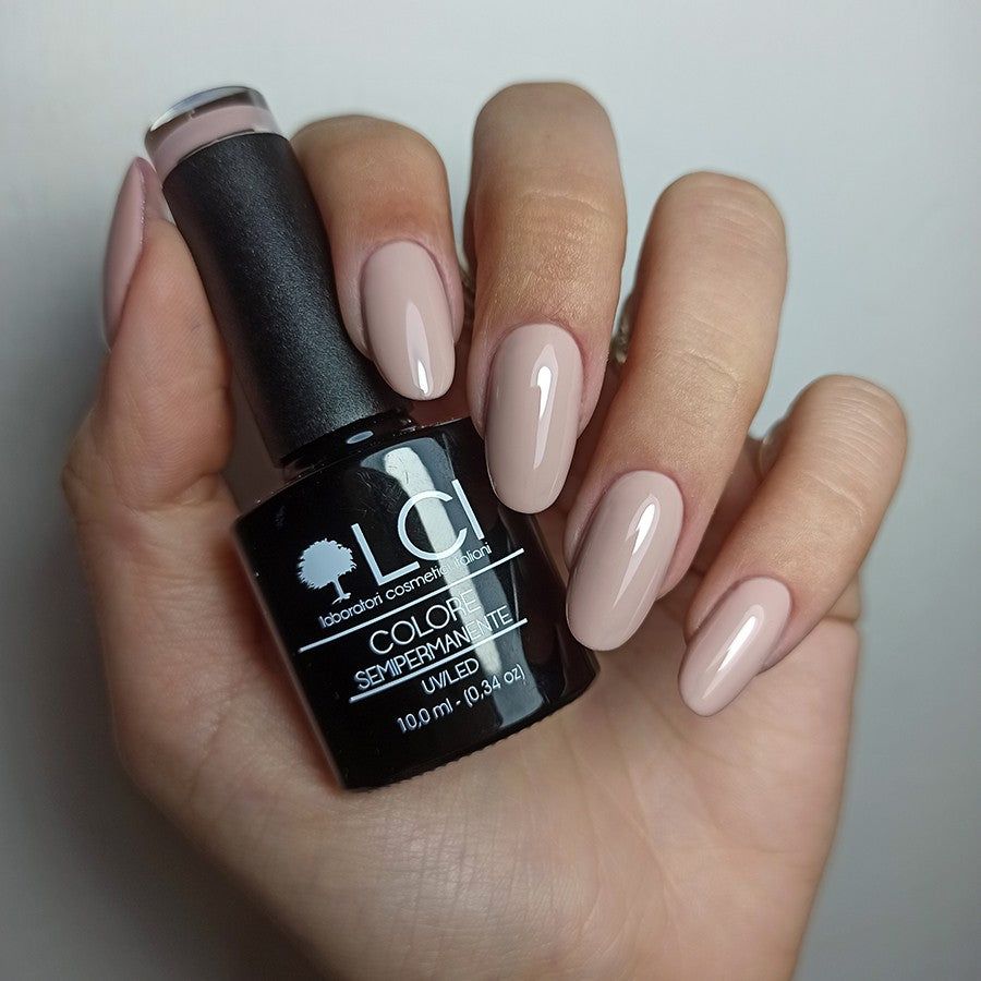 Mano con unghie smaltate e flacone di smalto. Unghie nude. Flacone nero con logo e testo bianchi.