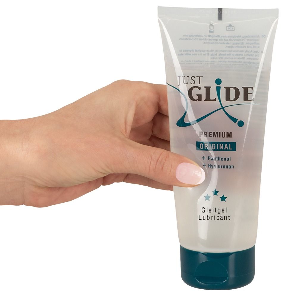 Mano che tiene un tubo di gel lubrificante. Scritta: Just Glide, Premium Original. Contiene pantenolo e ialuronano. Tappo blu.
