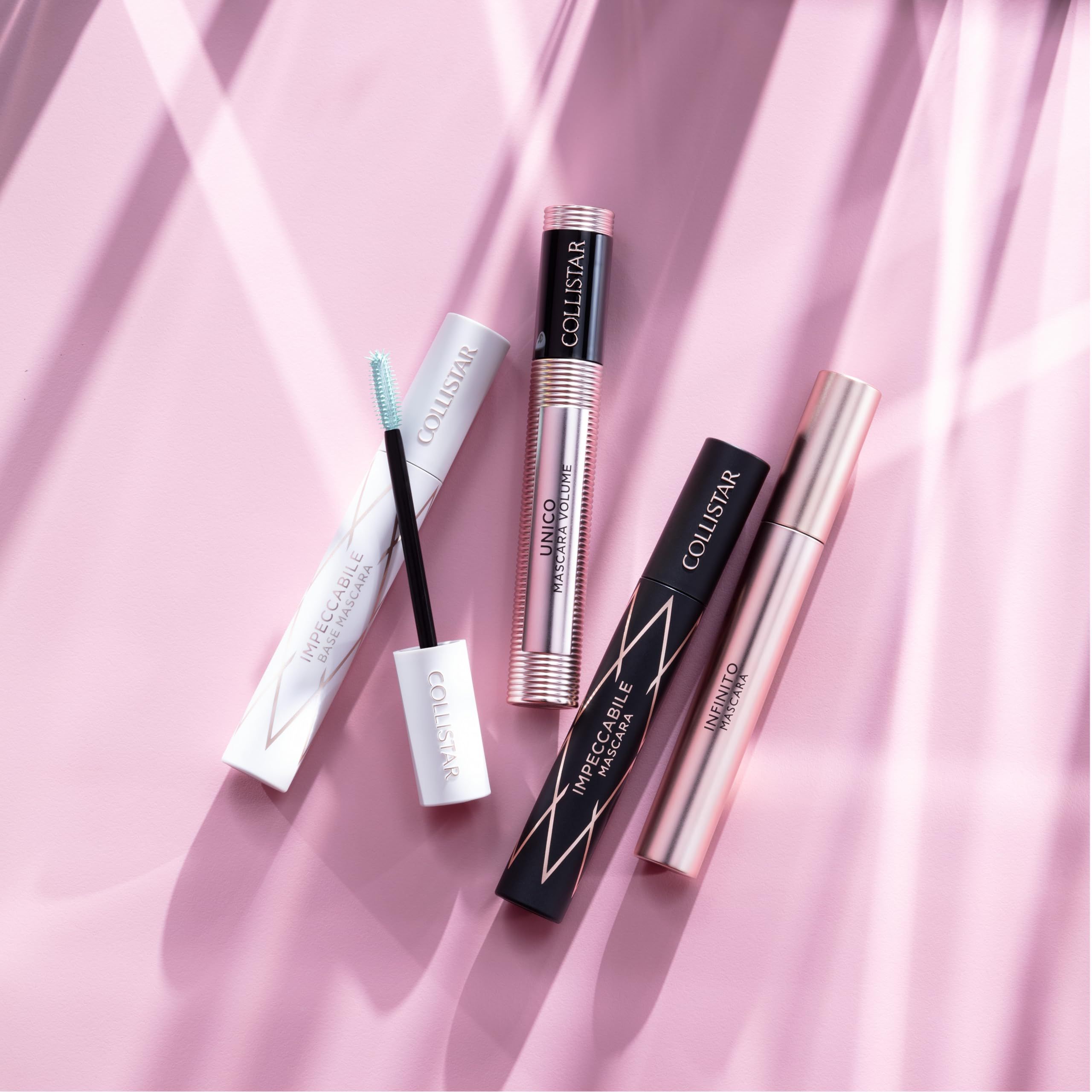 Diversi mascara su sfondo rosa. Vari contenitori, tra cui primer e mascara.