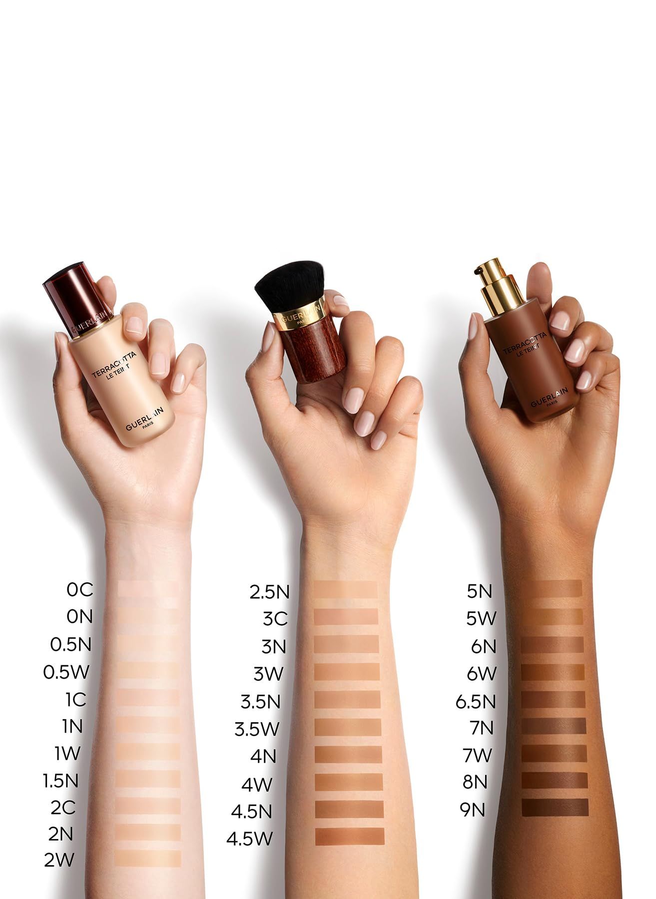 Mani mostrano le tonalità del fondotinta Guerlain Terracotta Fluido. Diverse tonalità della pelle con campioni. Flaconi e pennello.